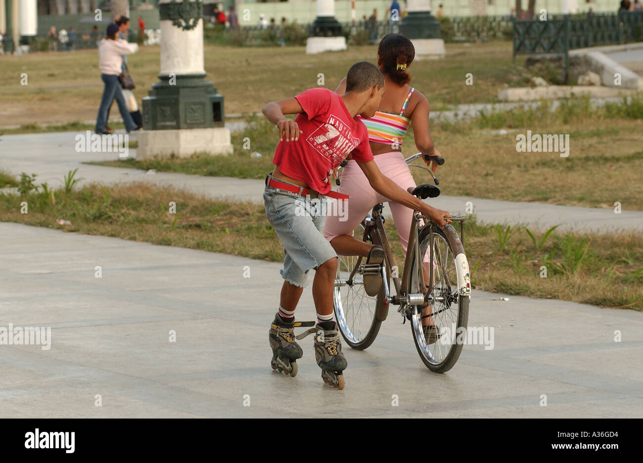 Boy on inline skates holding on to a bicycle ridden by a girl Havana Cuba Stock Photo