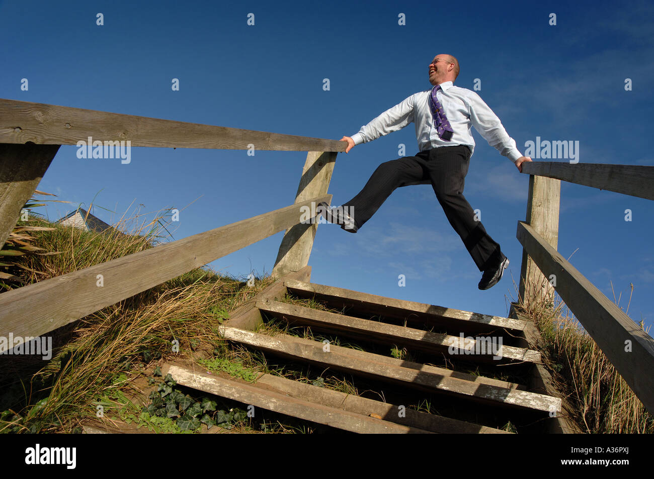 a man in a suit standing at the top of a set of stairs with a clear blue sky behind Stock Photo