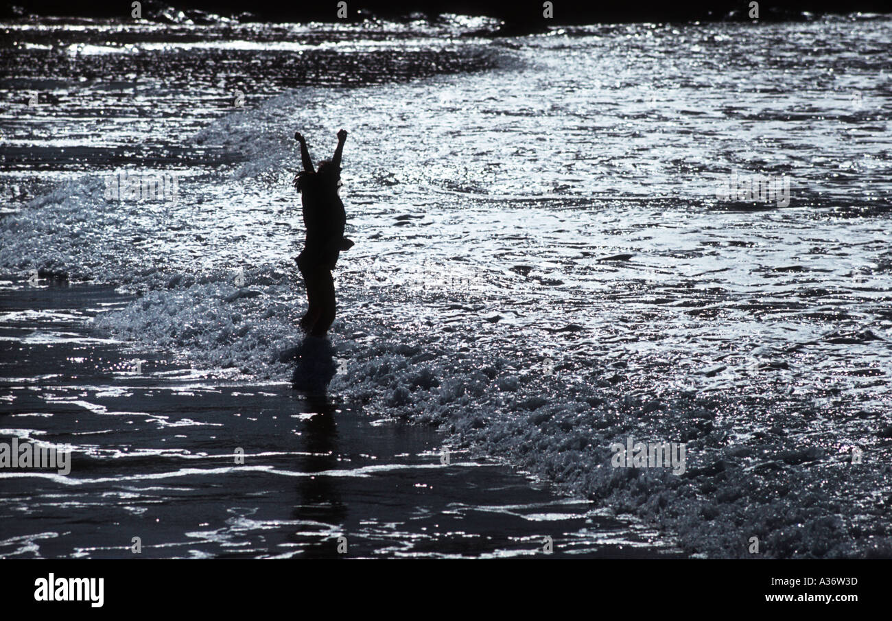 Child wading in the sea silhouette raising her arms Stock Photo