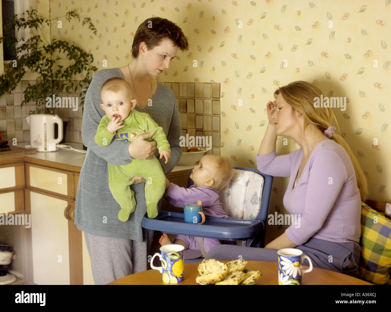 Depressed looking mother with a child listens whilst another mother talks to her in the kitchen Stock Photo