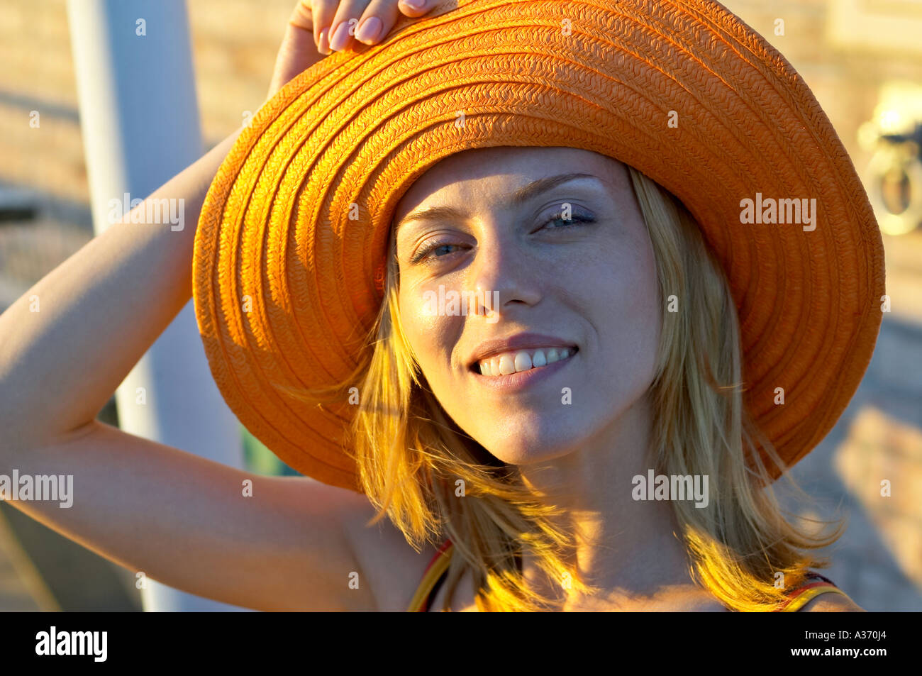 Portrait of a pretty and young Caucasian woman holding her summer hat. Smiling in the sunlight. Stock Photo