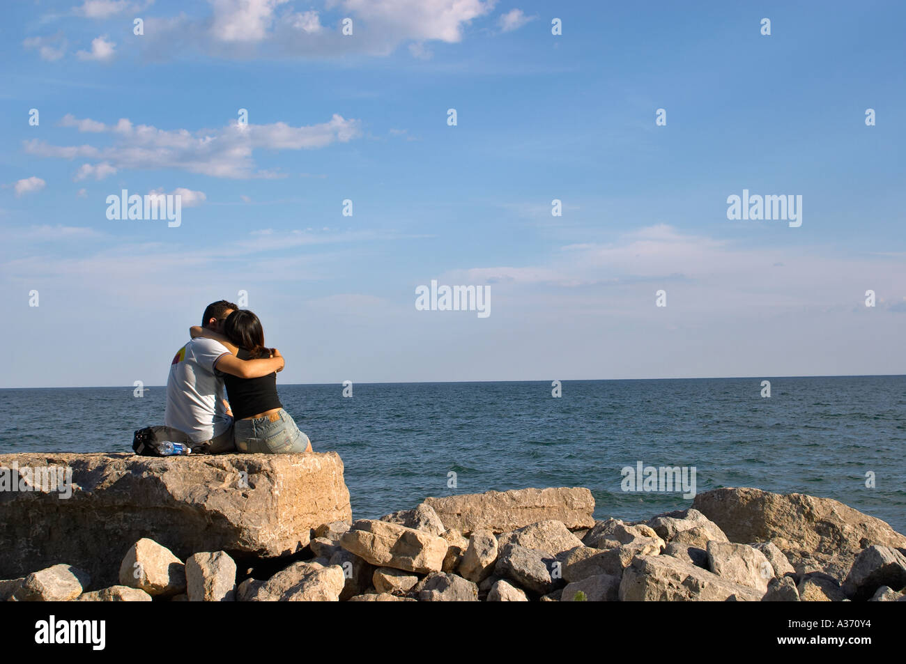 Couple - man and woman - sitting on the rocks by the water, locked in an embrace. Stock Photo