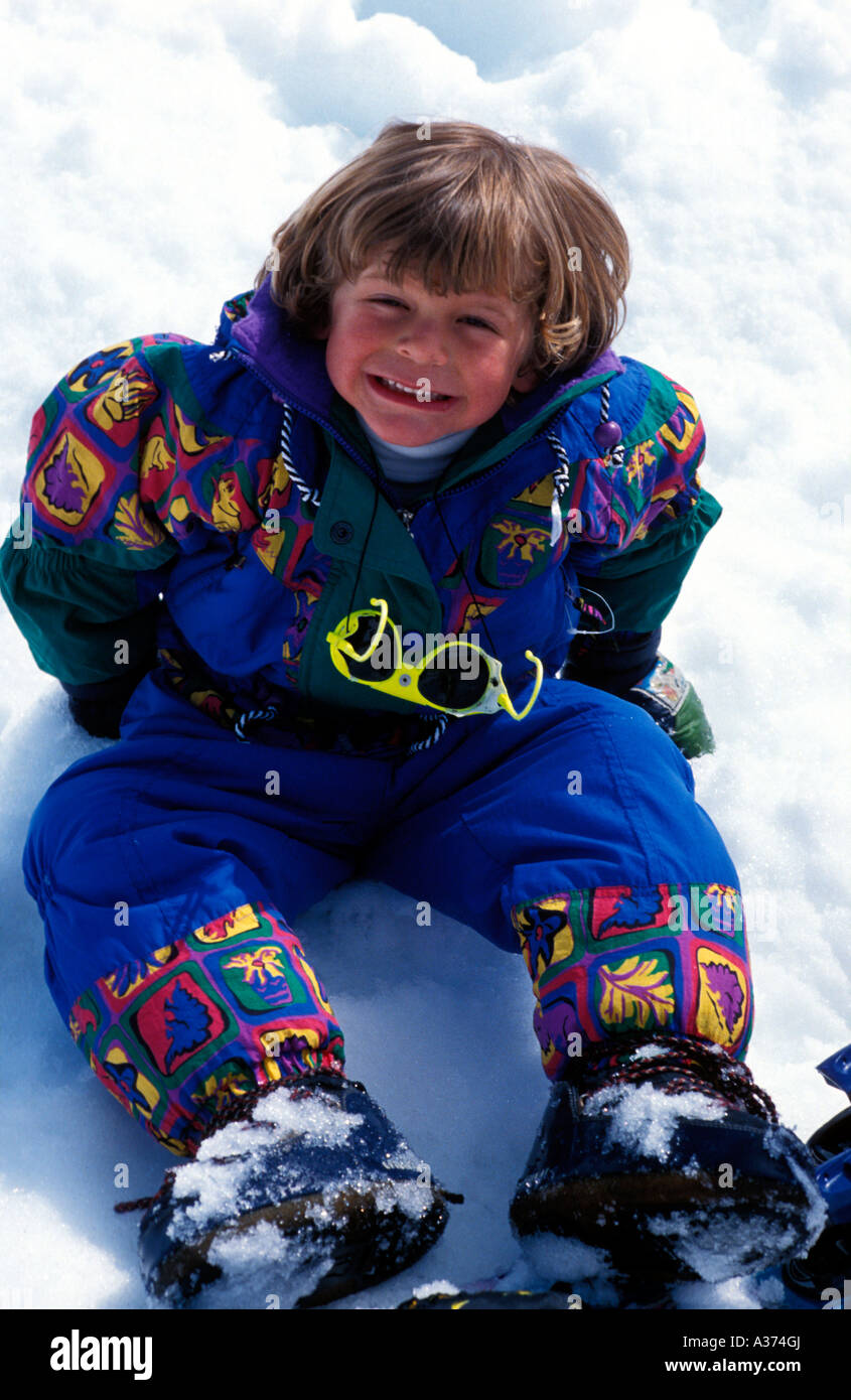 Small boy sitting in the snow in ski suit with snow boots Stock Photo