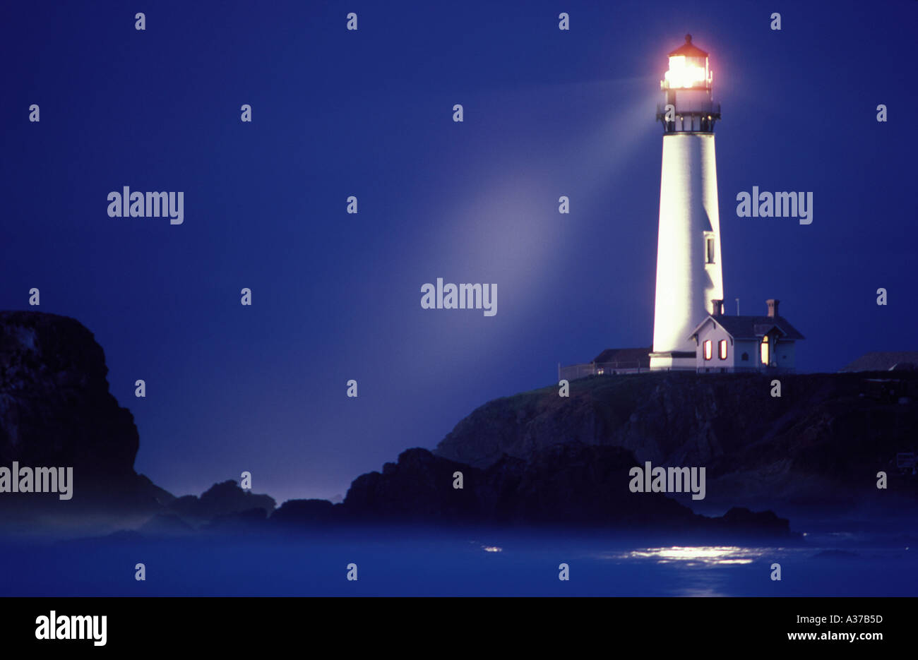 Pigeon Point Lighthouse casting beam across rocky shore at dark dawn sky. Image is not digitally altered - No photo shop.  REAL! Stock Photo
