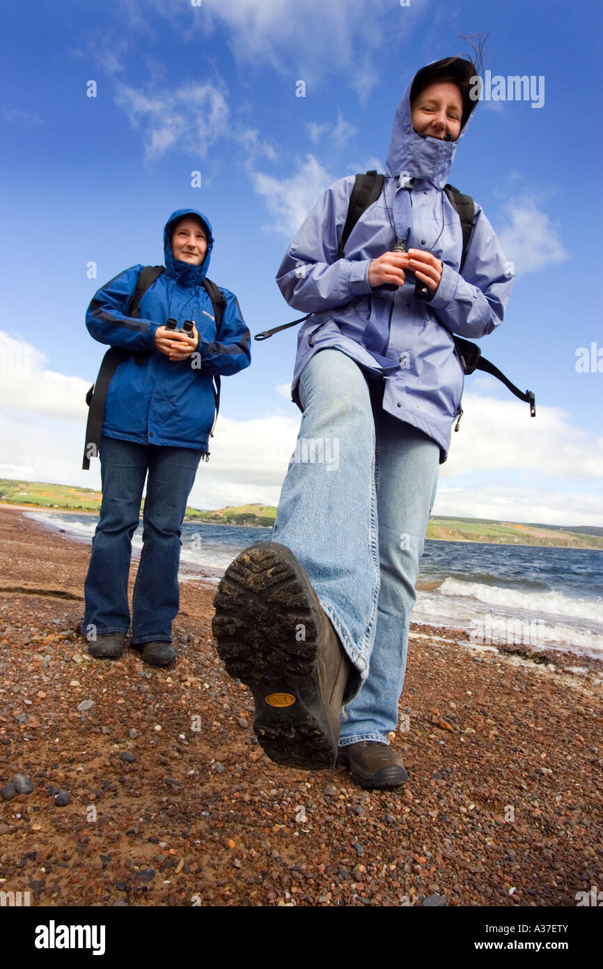 Two girl hikers walking in the sunshine along the shore at Rosemarkie Moray Firth Stock Photo