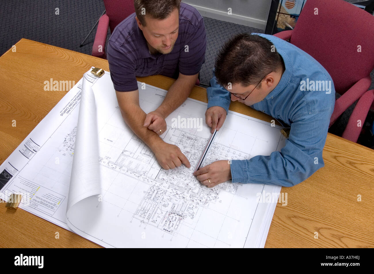 Shot from above as two men review blueprints on a large wood desk Stock Photo