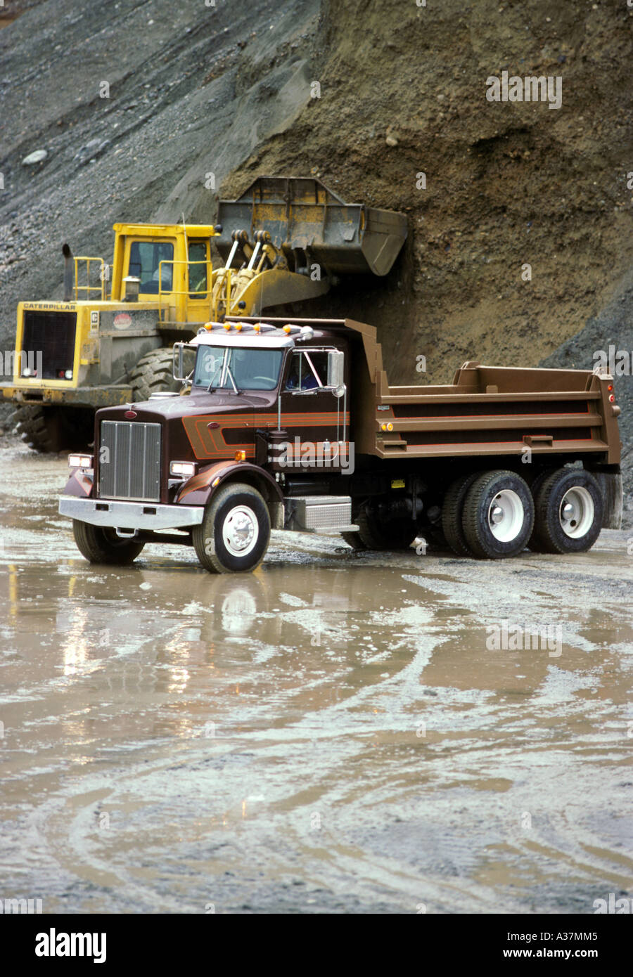 A new dump truck awaits a load of gravel from a front loader Stock