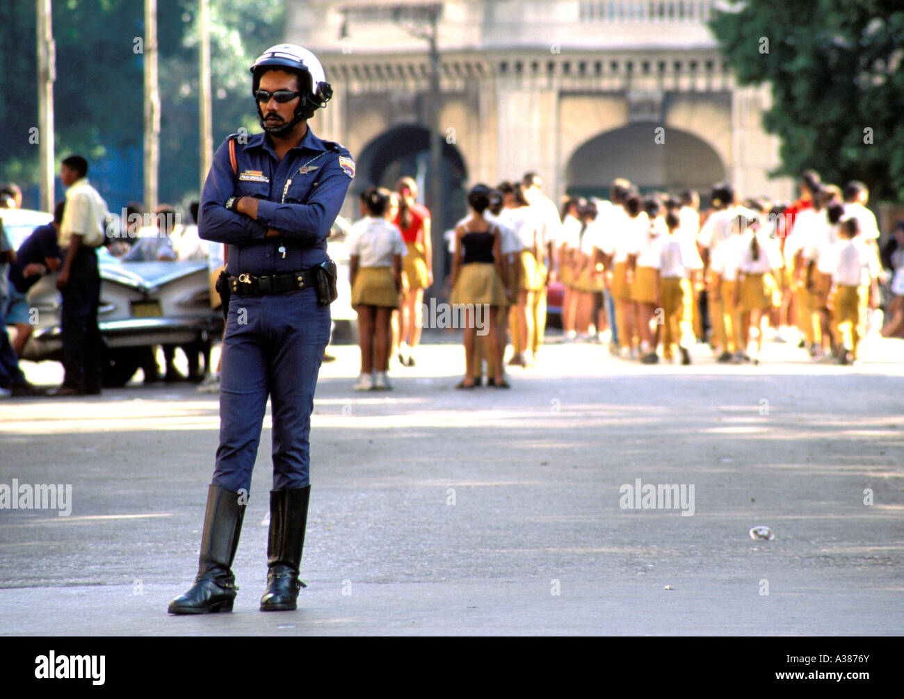 A policeman stands guard in Central Havana while shool children practice marching in the background Stock Photo