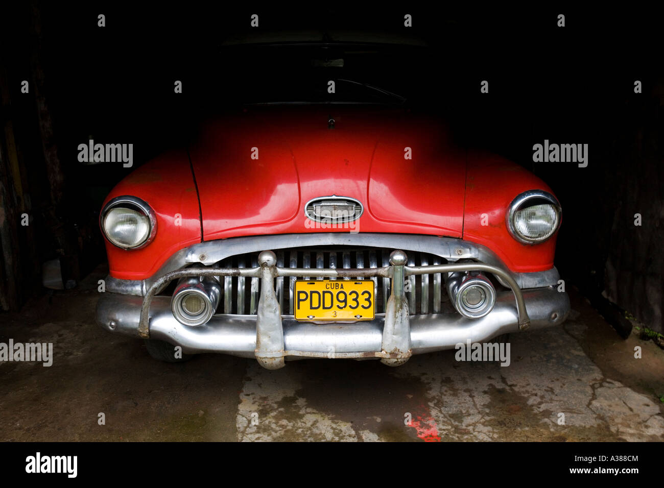 A red classic American car sits in the shadow of a garage in Vinales Stock Photo
