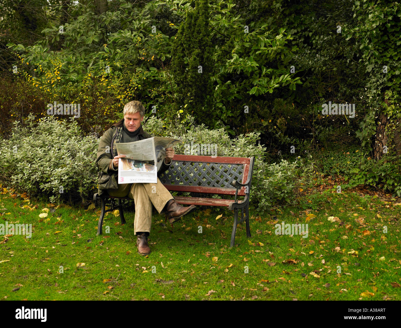 man reading newspaper on park bench Stock Photo - Alamy