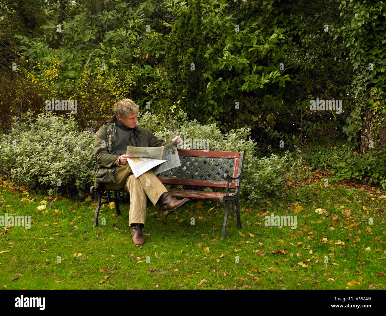 man reading newspaper on park bench Stock Photo - Alamy