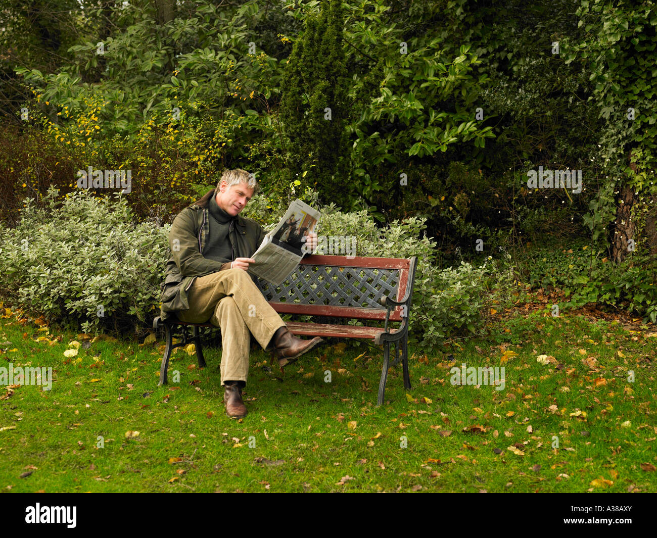 man reading newspaper on park bench Stock Photo - Alamy