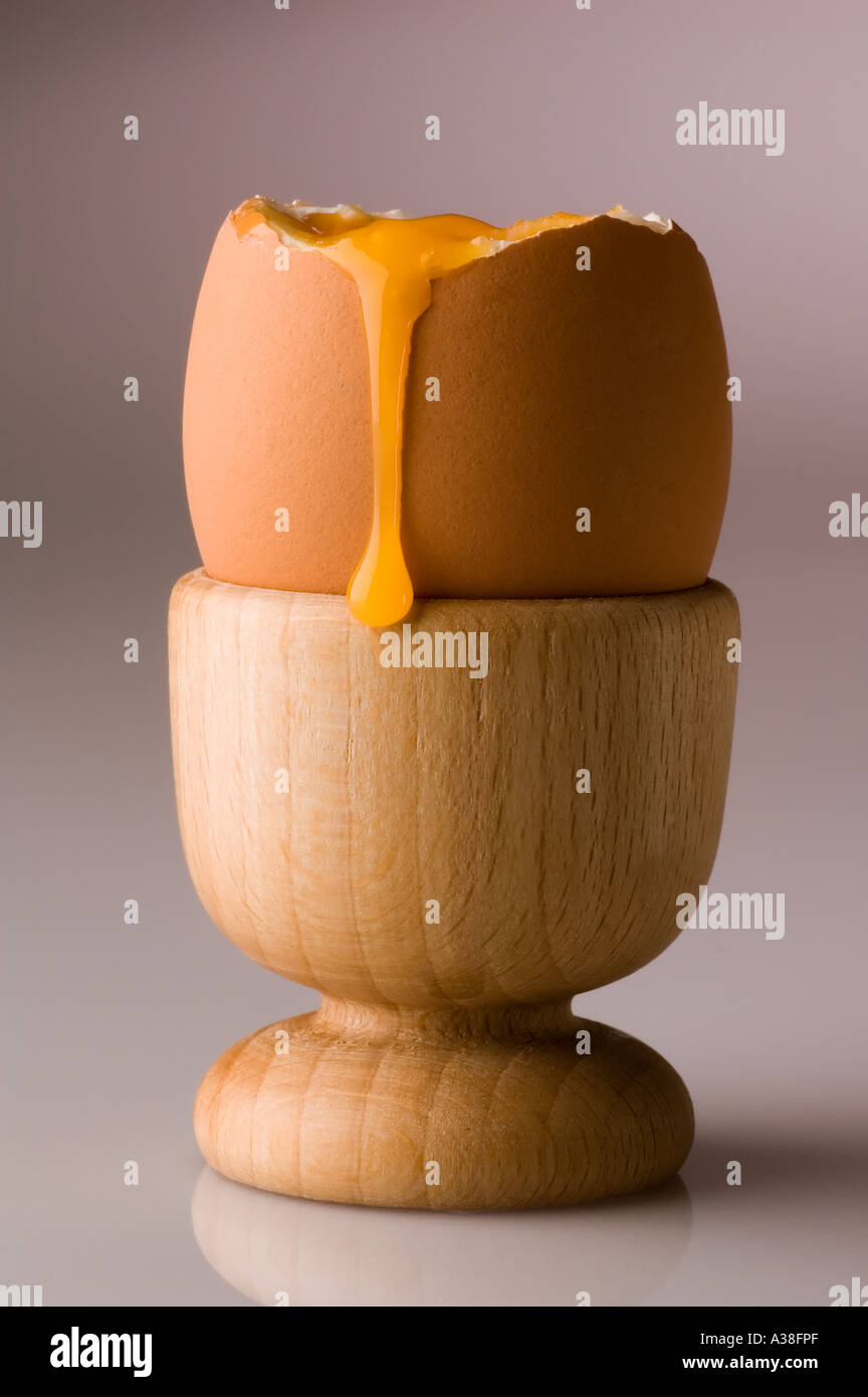 A soft boiled egg in a wooden egg cup with yoke running down the side