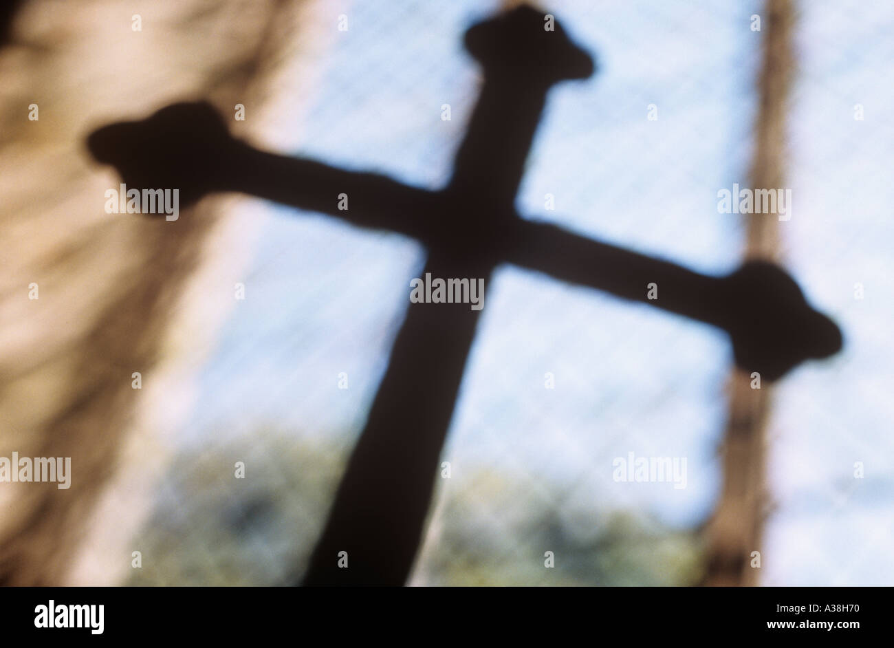 Defocussed crucifix silhouetted against large plain diamond leaded window Stock Photo