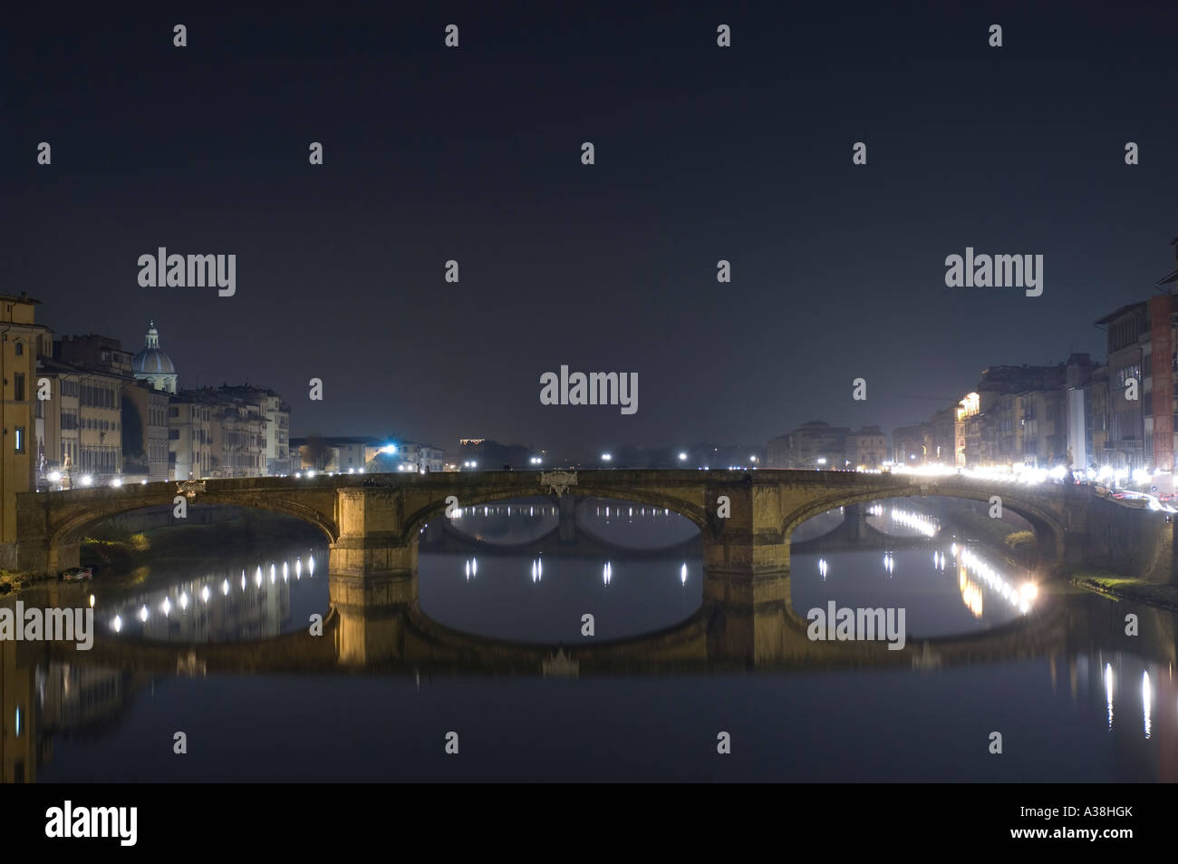 A view of the Ponte Santa Trinita (bridge) reflected in the calm water of the Arno river in Florence at night. Stock Photo