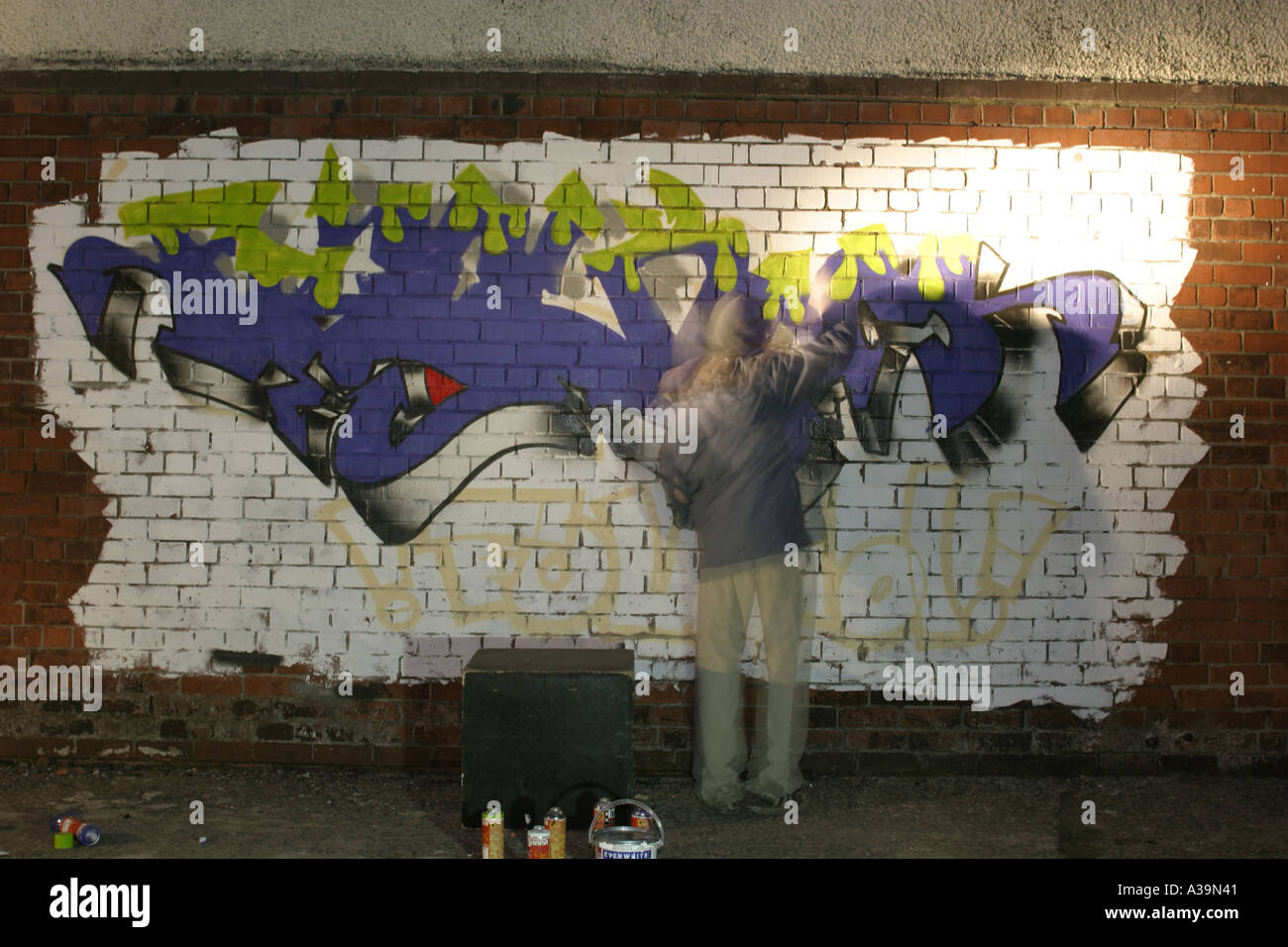 Graffitti Tag artist at work with spray paint can wearing hooded top