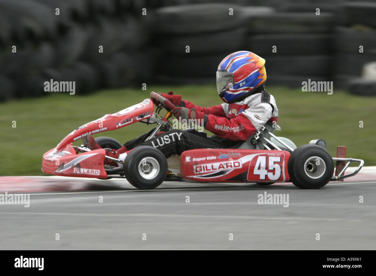 junior jnr rotax max kart driver blurs over a kerb with tyrewall in the background at Nutts Corner Motorsport Circuit Stock Photo