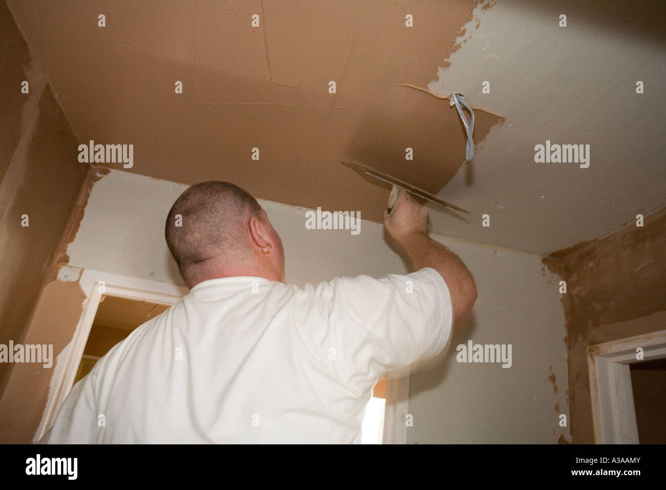 A Plasterer Applying Skim Layer To A Dry Lined Ceiling In A