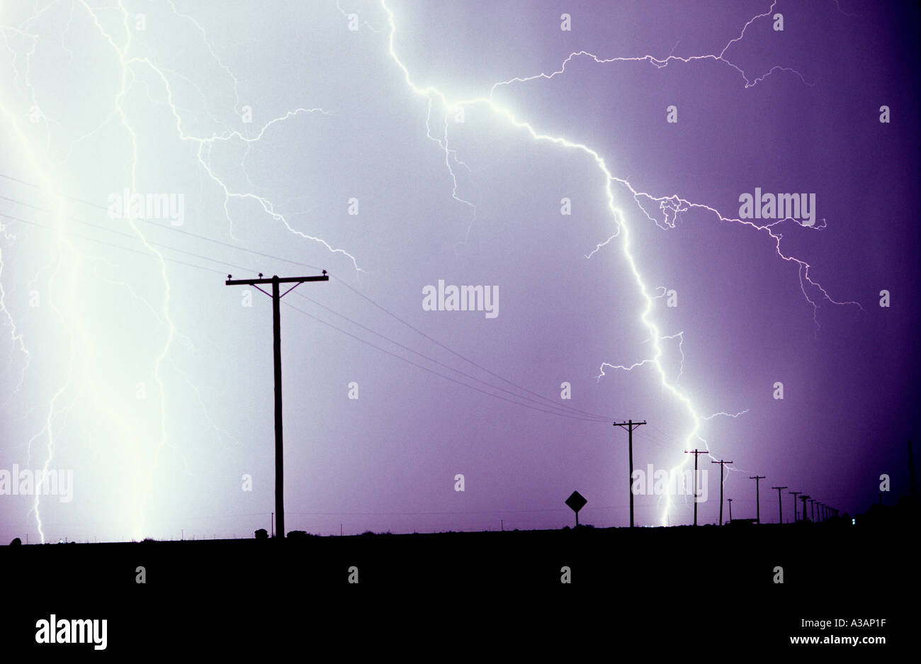 Lightning strikes from a purple sky near powerlines and power poles in
