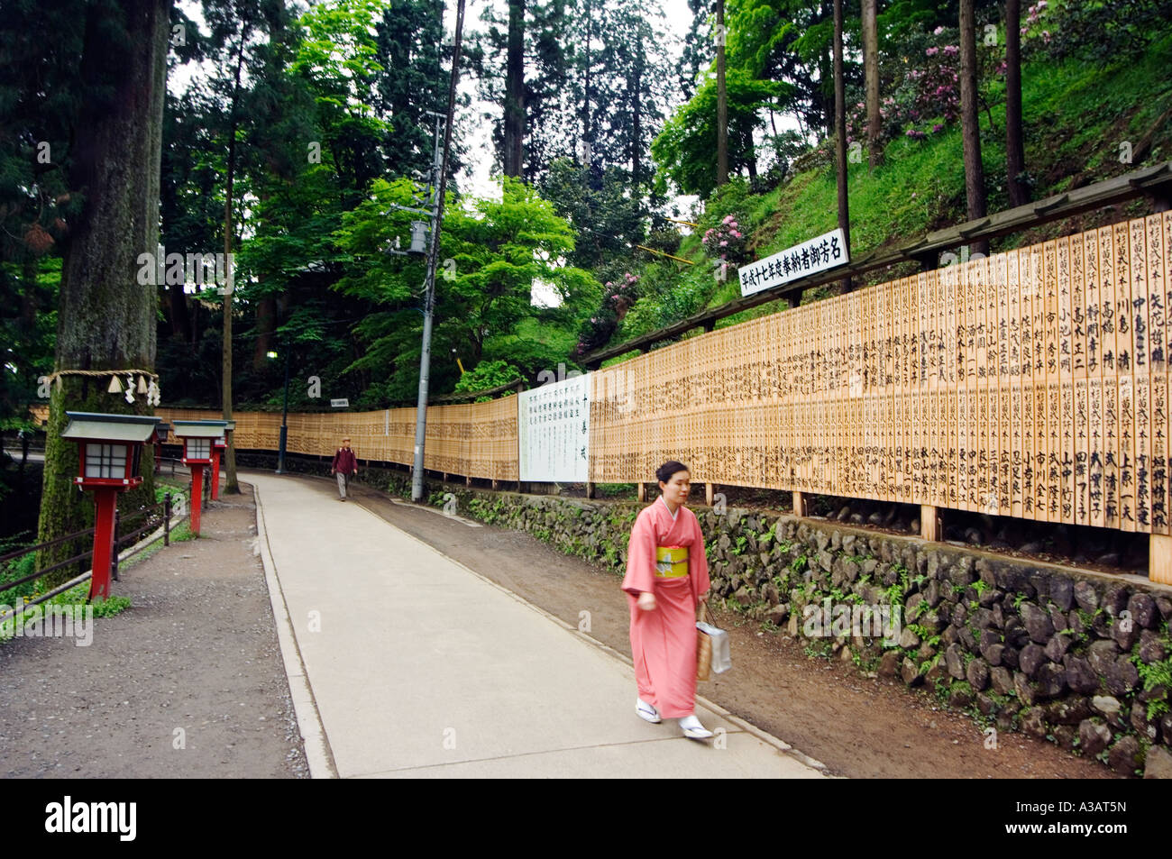 woman in pink kimono row of plaques displaying list of shrine sponsor wirtten in chinese charachters red lanterns on path Takao Stock Photo