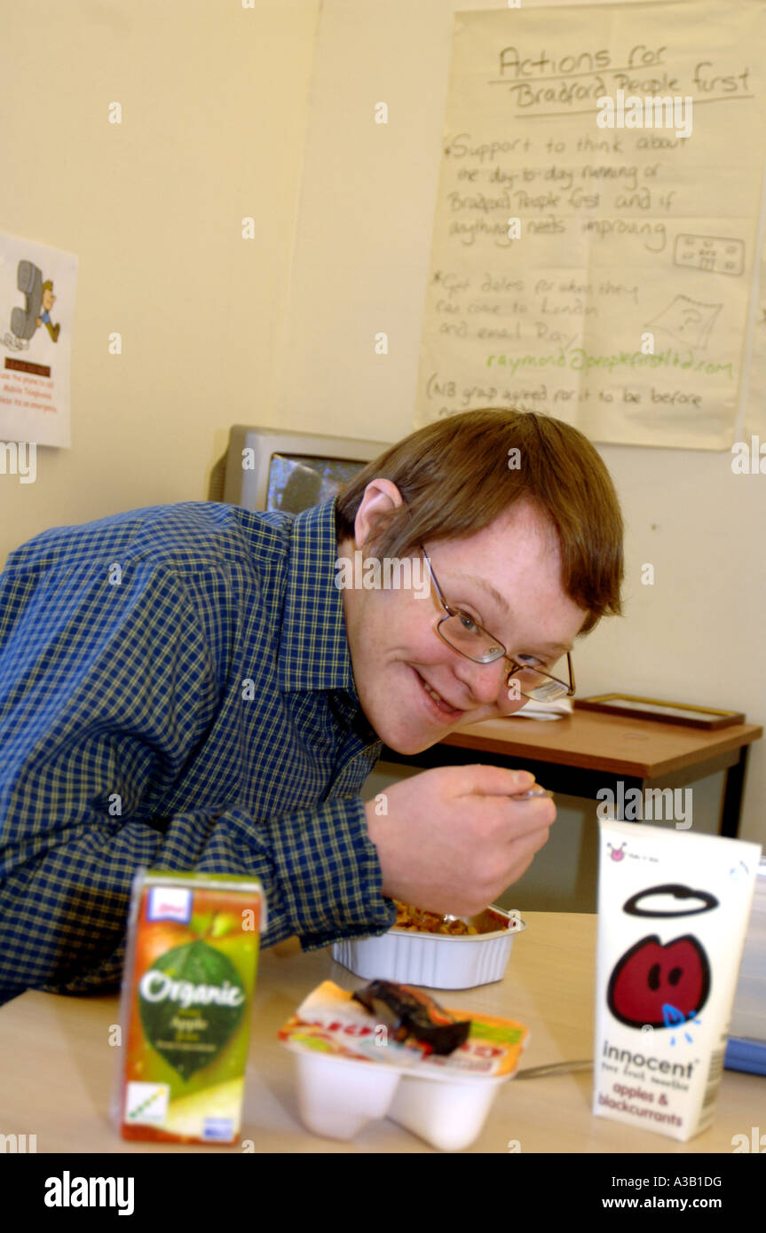 A man with downs syndrom eats his dinner with his group in a community centre kitchen Bradford West Yorkshire MODEL RELEASED Stock Photo