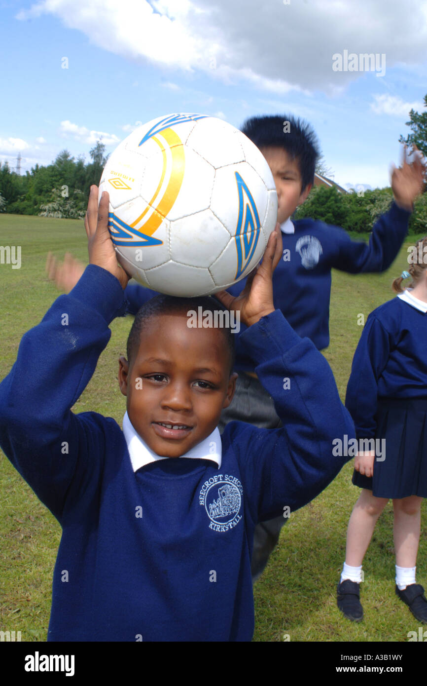 Mixed group of primary school children play football on the school playing field Stock Photo