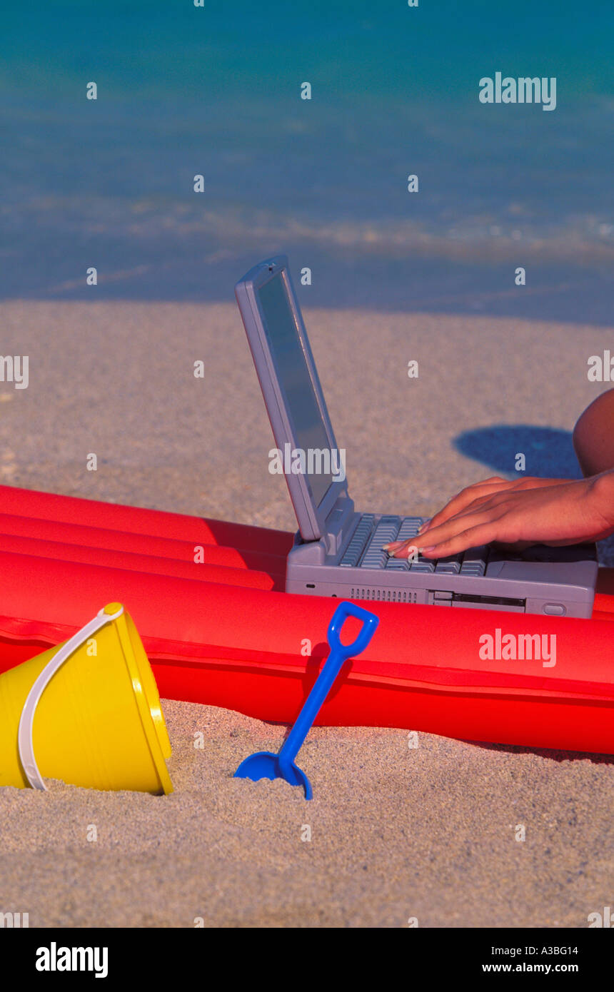 Hand typing on Notebook computer with floating mattress and beach toys by the beach 2803 015 22 Stock Photo