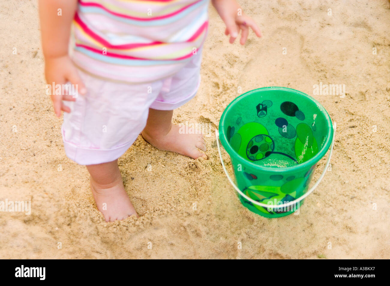 Toddler (18-24 months) standing on beach with toy bucket, low section Stock Photo