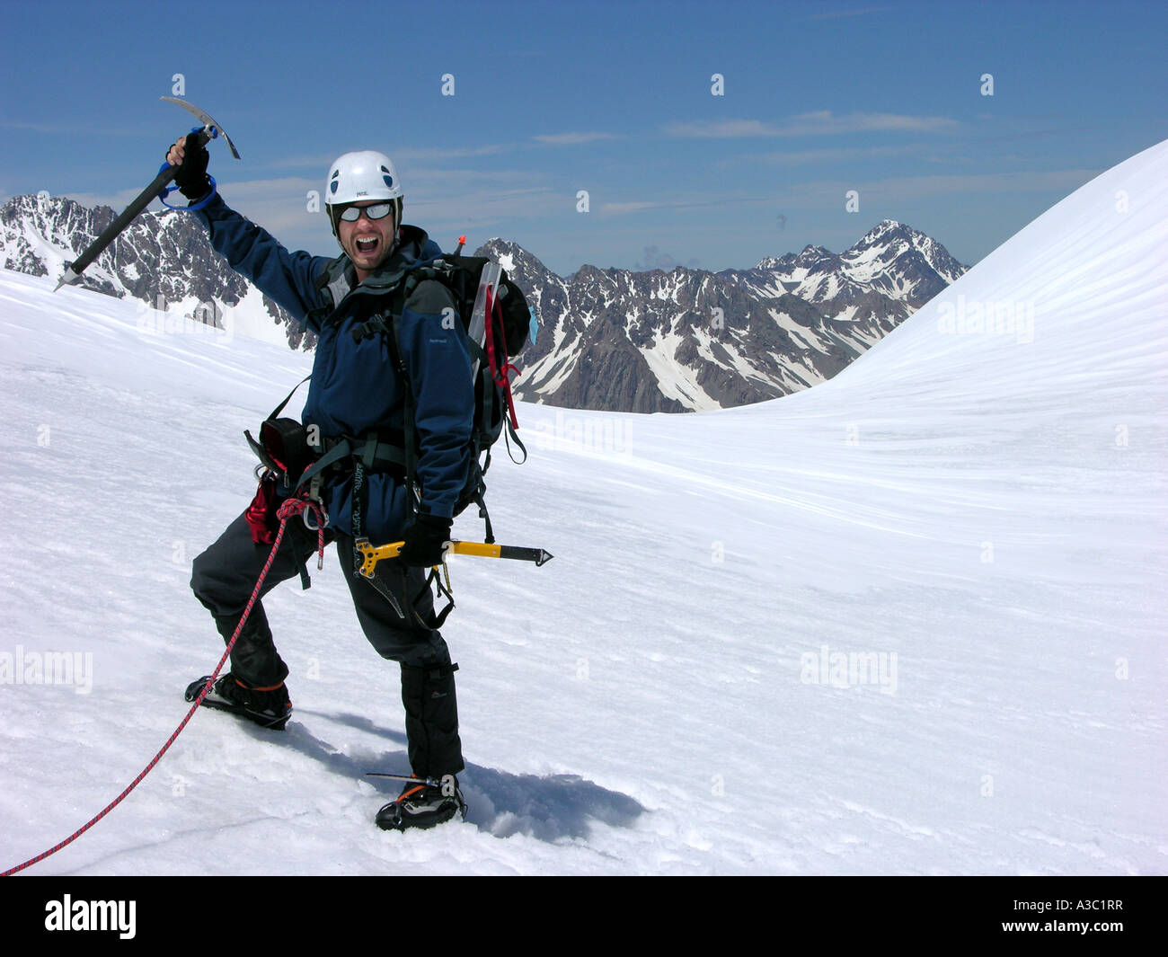 A happy mountain climber raises his ice pick and smiles as he crosses ...
