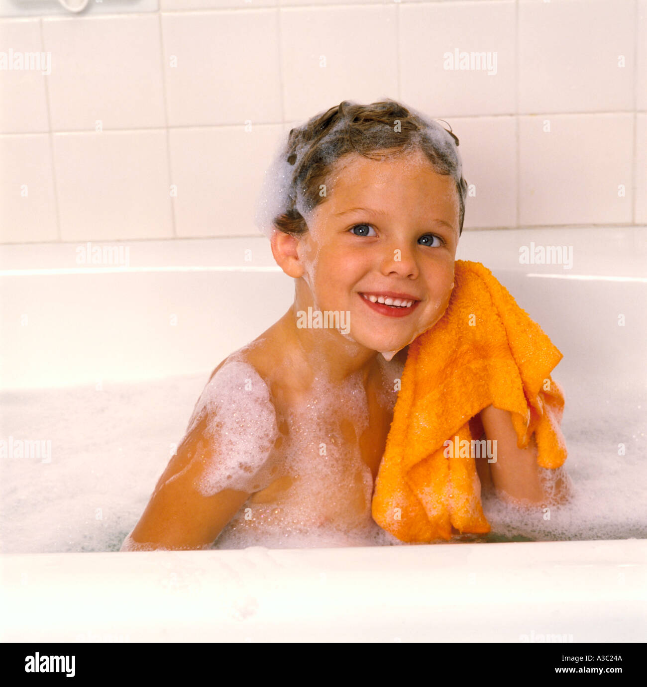 Little boy taking a bubble bath with shampoo in his hair and is wiping