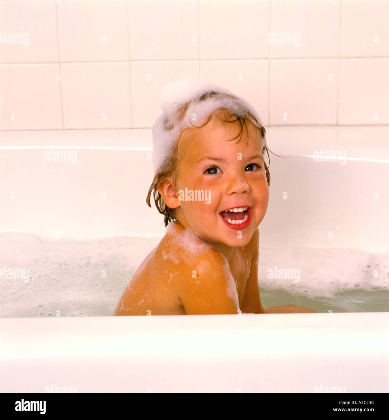 A smiling little girl taking a bubble bath with shampoo in her hair and