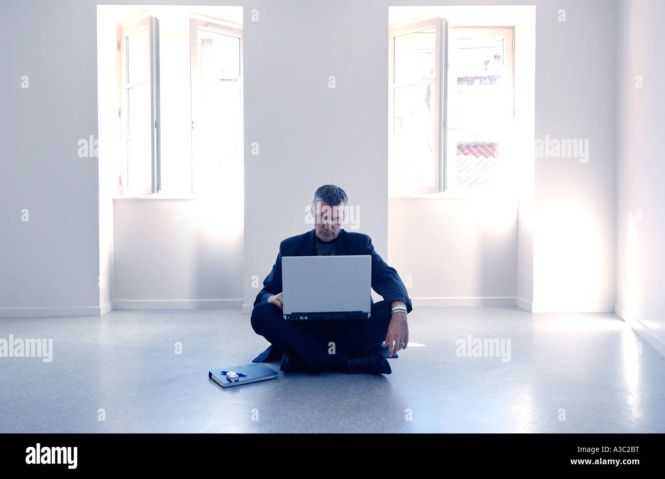 Man with laptop computer sitting on the floor alone in the middle of a white empty room Stock Photo