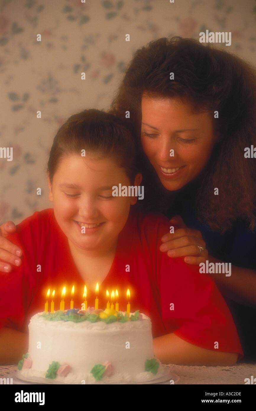 A young girl celebrating her 12th birthday by preparing to blow out candles on her cake as mom observes Stock Photo