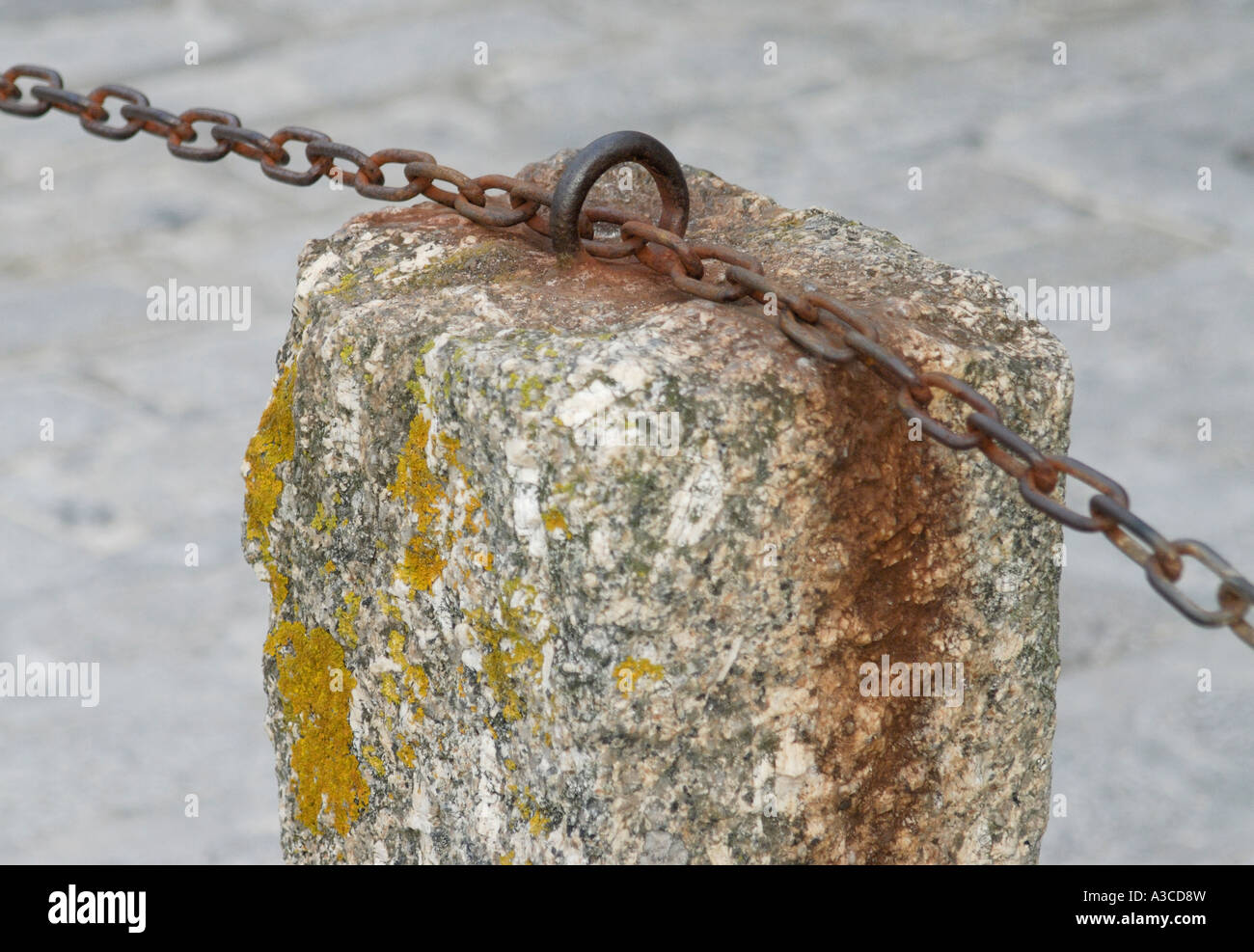 A granite bollard with a rusty iron chain running through a staple Rust