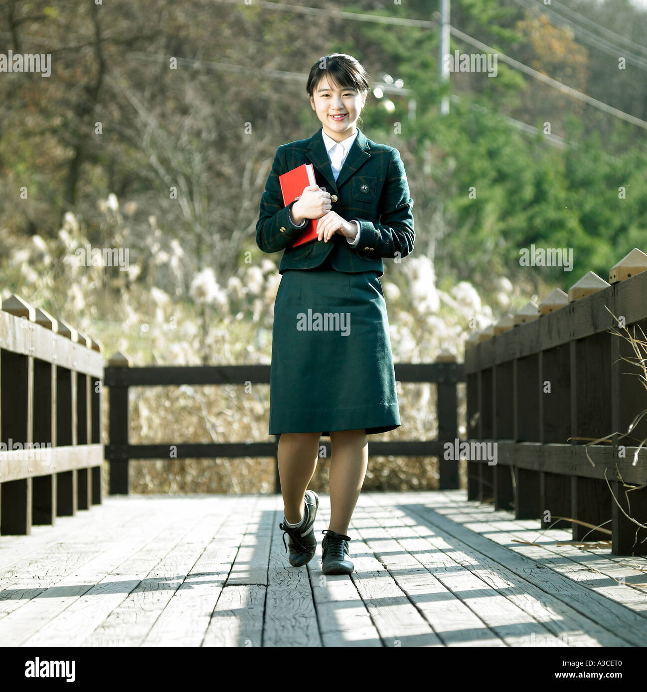 A female student in a school uniform is holding a book and walking Stock Photo