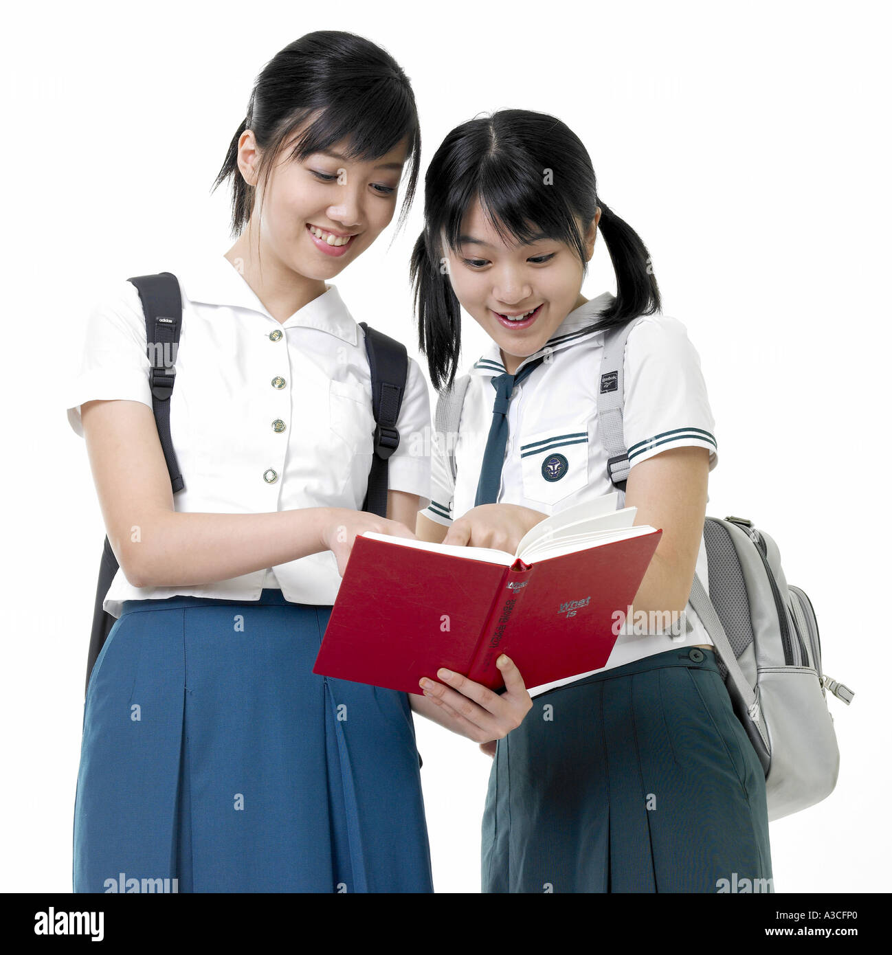 Two female students with back packs are reading a book Stock Photo