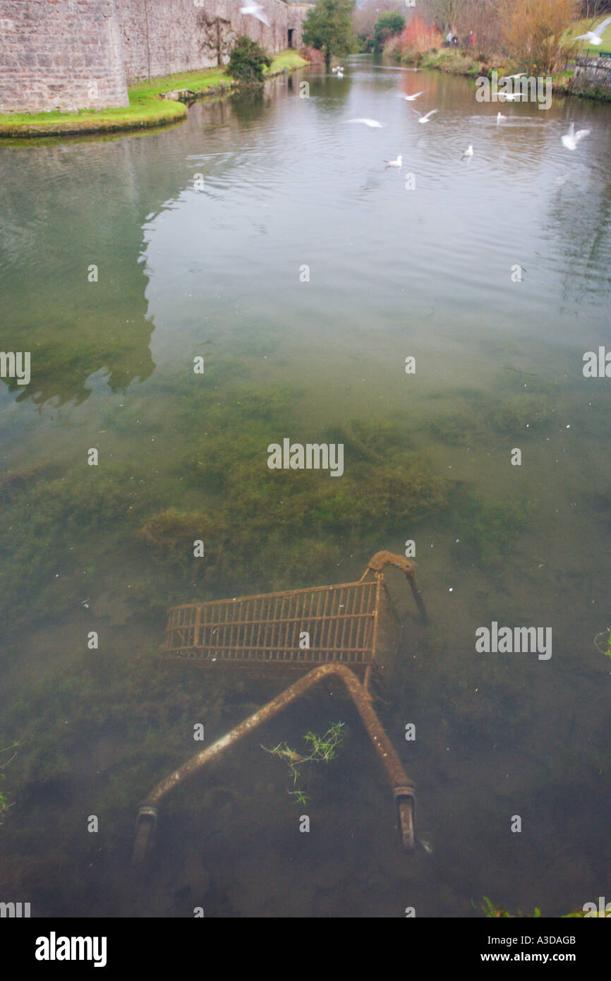 Thoughtless dumping resulting in lichen and weed covered supermarket trolley in moat of Bishops Palace in Wells England Stock Photo