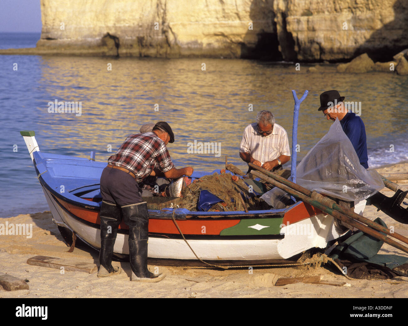 Carvoeiro Algarve Portugal beach Portuguese fisherman at work talking working together at colourful small fishing boat checking repairing fishing nets Stock Photo