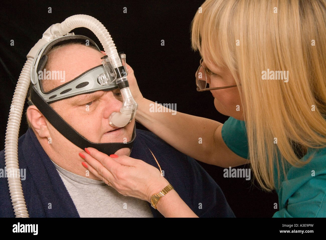 Nurse adjusts a CPAP machine on overweight patient. CPAP stands for Continuous Positive Airway Pressure Stock Photo