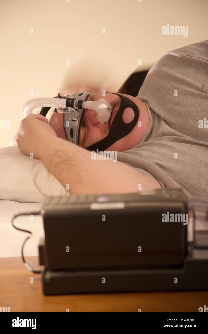 Overweight man tries to sleep while wearing a CPAP machine to bed. CPAP is Continuous Positive Airway Pressure. Stock Photo