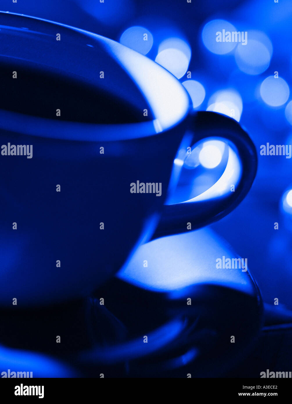Close up of Coffee Cup and saucer with city lights in background bathed in deep blue light. Stock Photo
