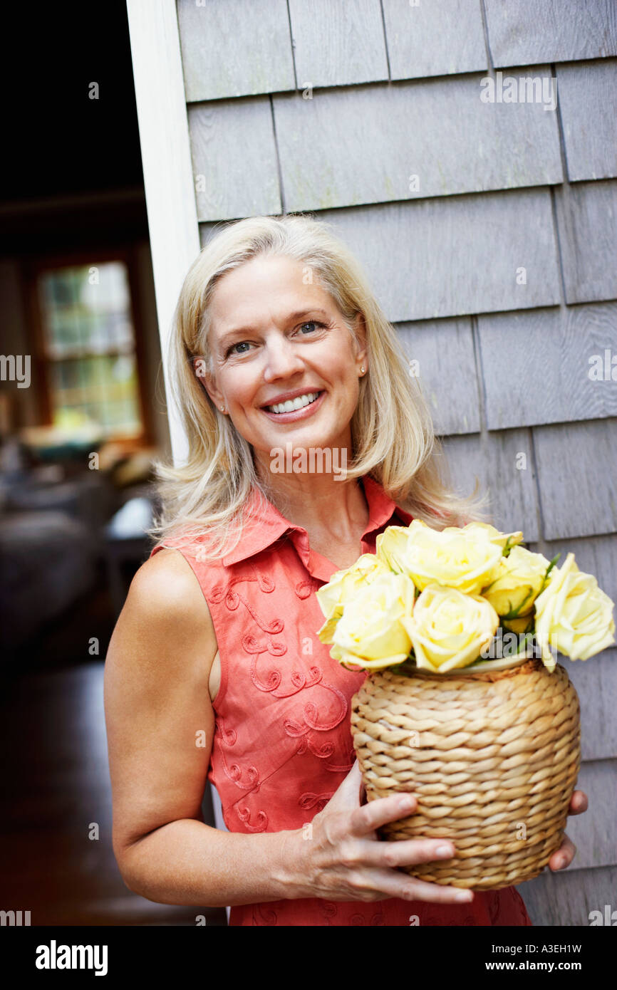 Portrait of a mature woman holding flowers in a vase and smiling Stock ...