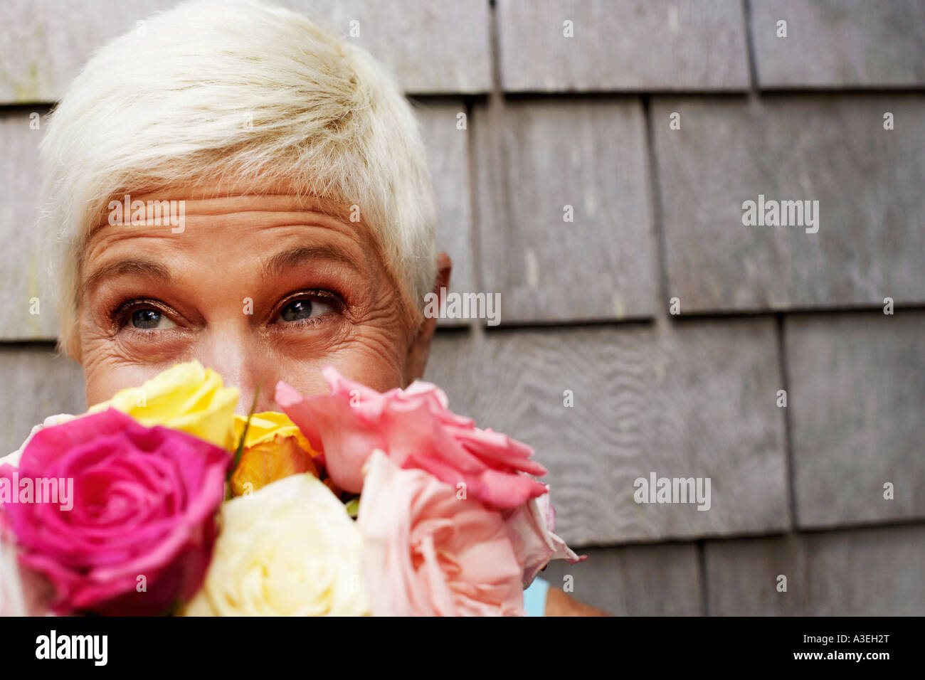 Close-up of a mature woman holding a bunch of flowers in front of her face and looking up Stock Photo