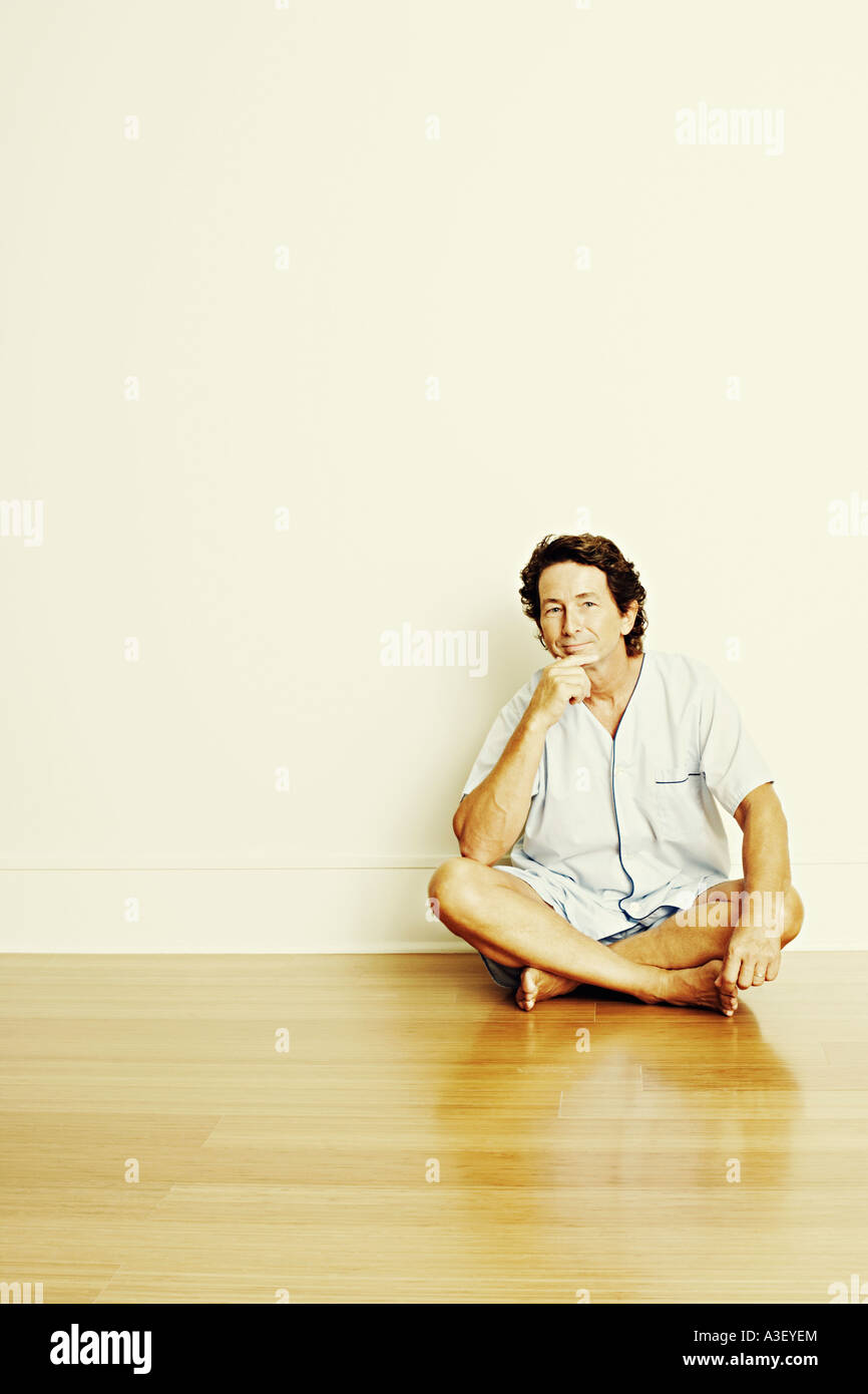 Portrait of a mature man sitting cross-legged on the floor and thinking ...