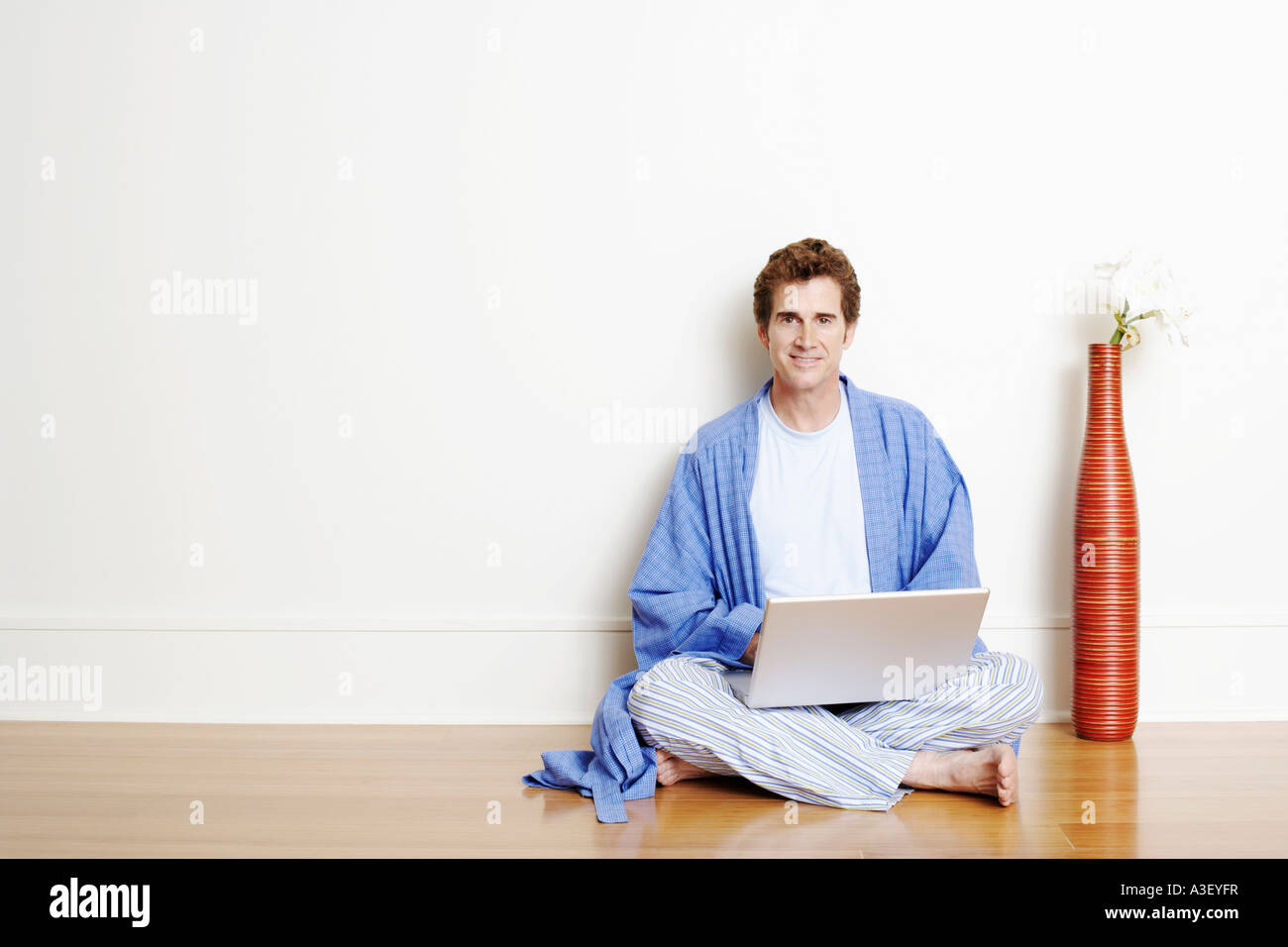 Portrait of a mature man sitting cross-legged on the floor and using a ...