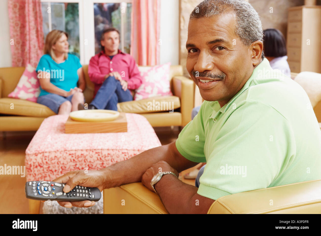 Portrait of a mature man operating a remote control with three mature people sitting beside him Stock Photo