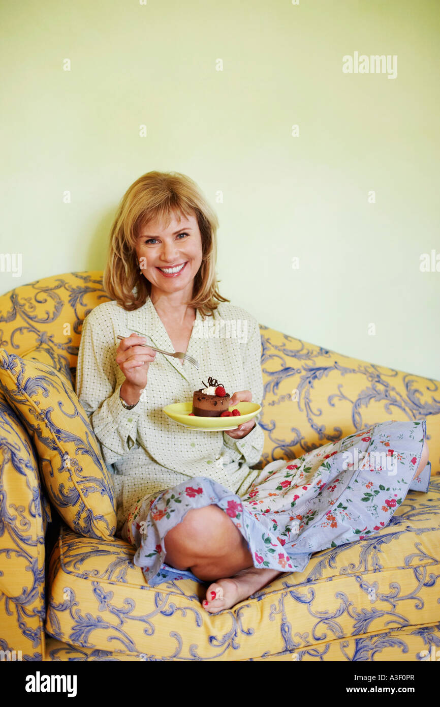 Portrait of a mature woman sitting on a couch and eating cake Stock ...