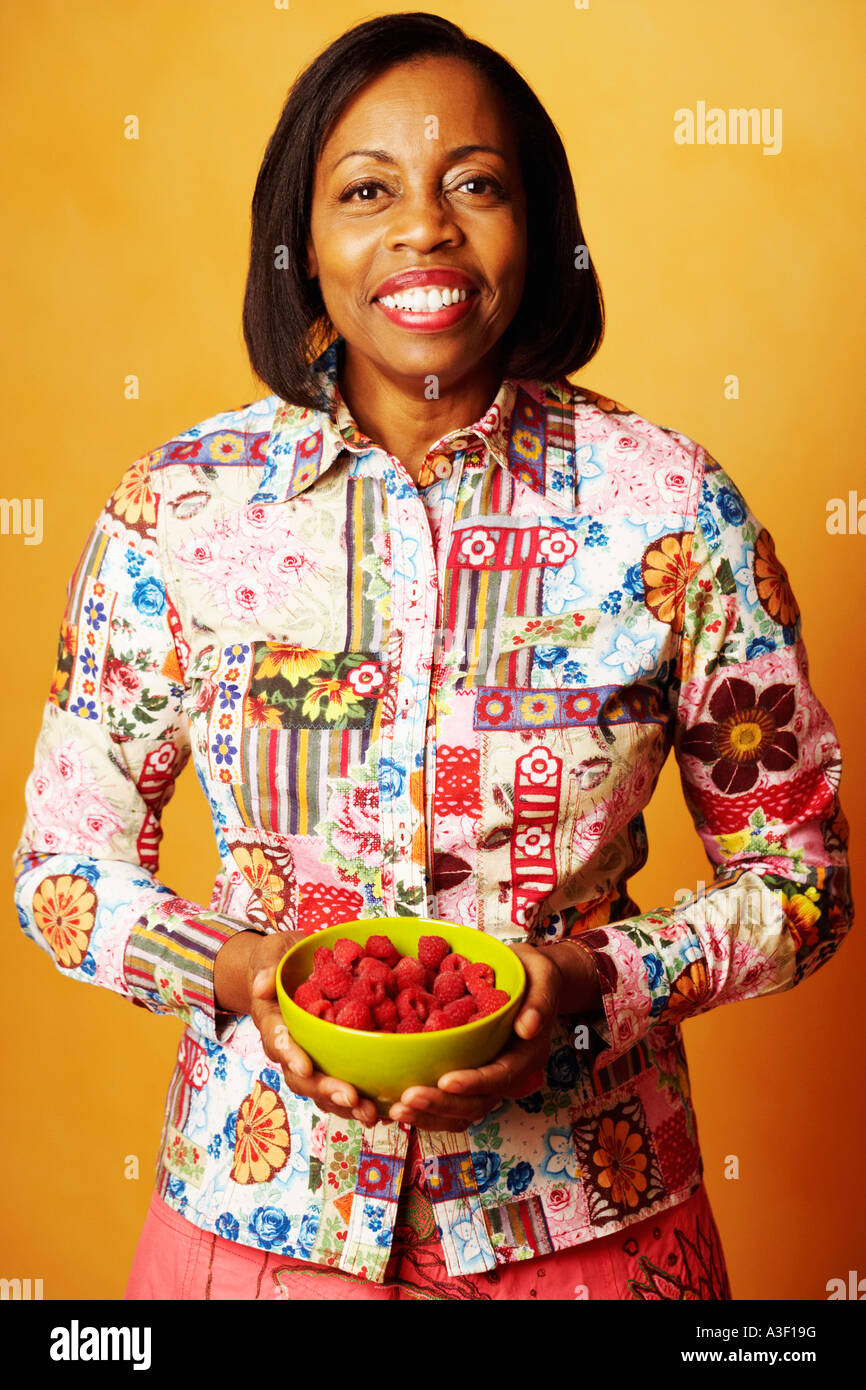 Portrait of a mature woman holding a bowl of raspberries and smiling ...