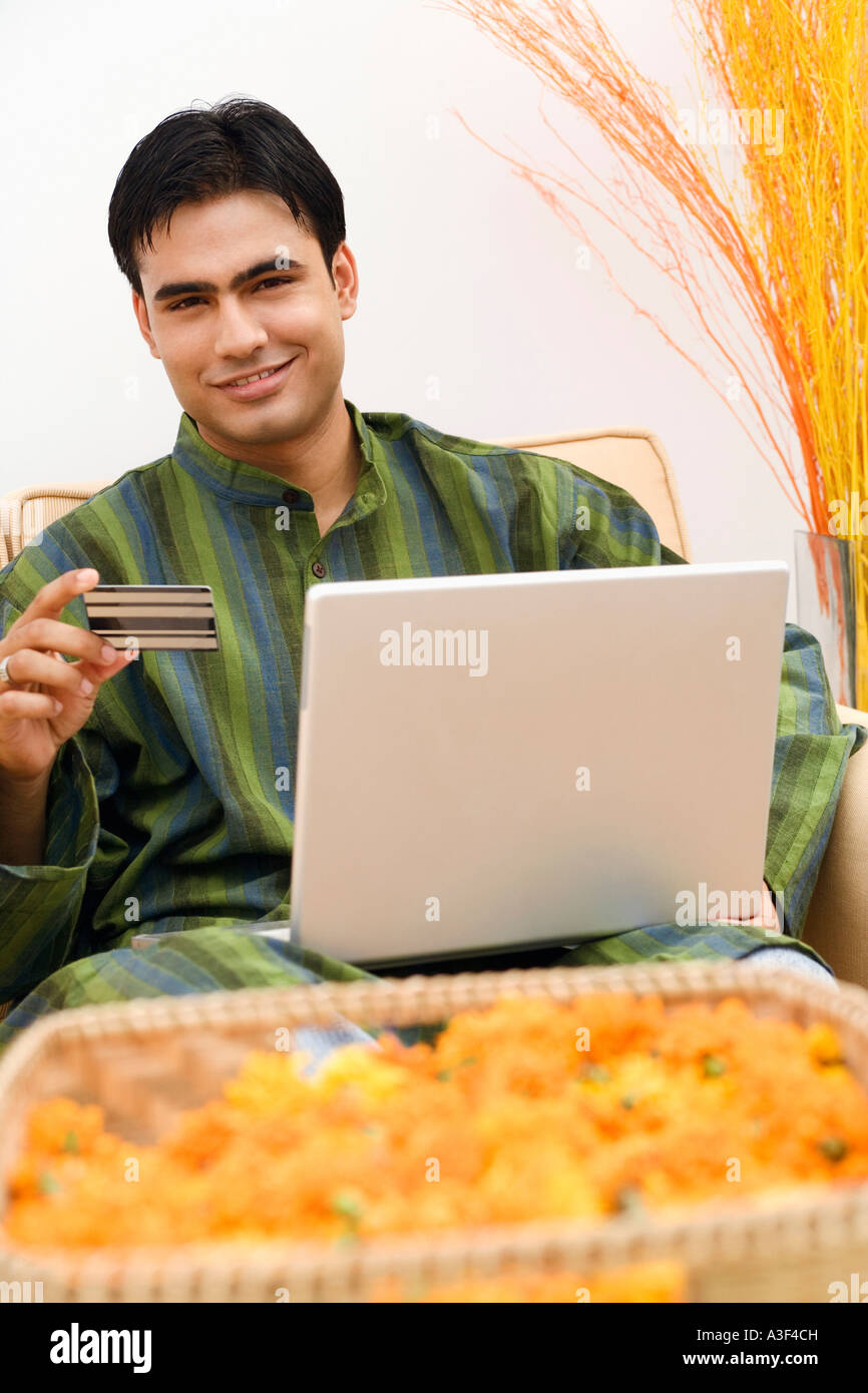Portrait of a young man holding a credit card with a laptop on his lap Stock Photo
