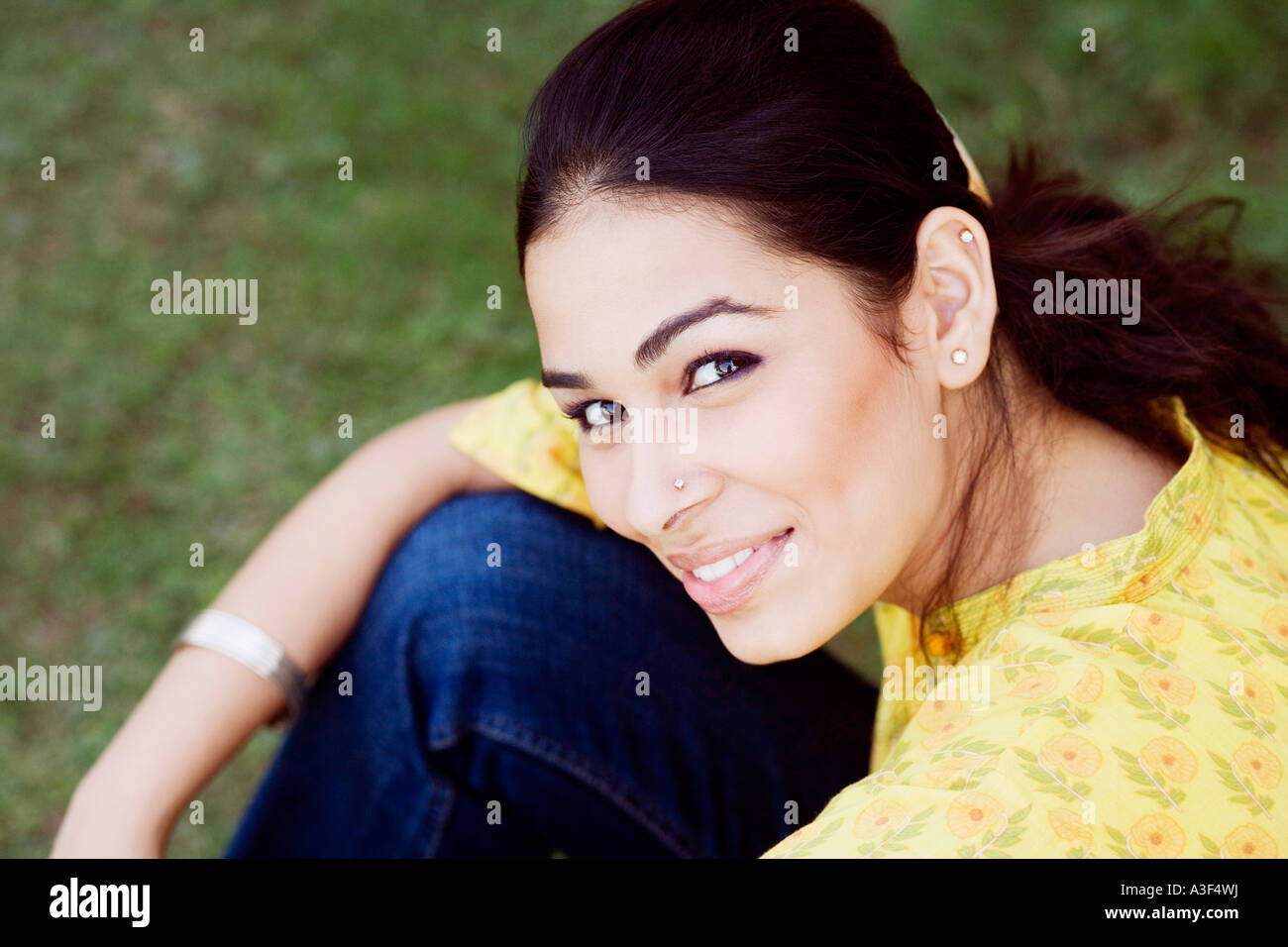 Portrait of a young woman sitting in a lawn and smiling Stock Photo - Alamy